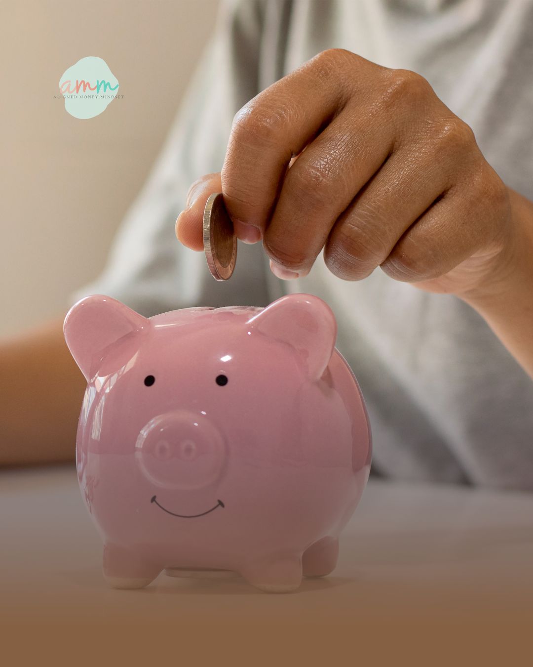 Person placing a coin into a pink piggy bank to build an emergency fund.